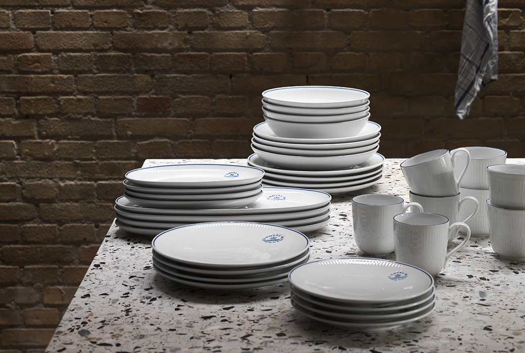 Stacked Blueline plates, mugs, and dishes on a kitchen table